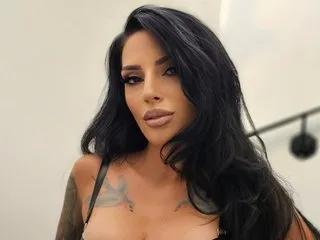 SarahHarries poses with long black hair and heavy makeup wearing a black strap top.