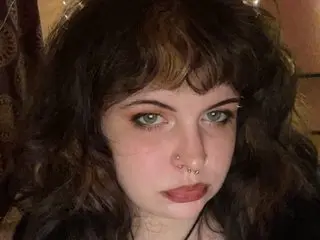 Young woman with wavy dark hair and nose piercings looking into the camera in a moody indoor setting.