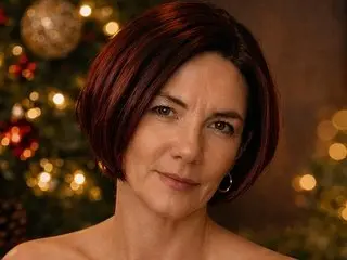 SashCarter poses with a slight smile, showing her short dark hair and bare shoulders against a warm, blurred background.