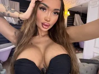 SashaFererra poses with long brown hair, wearing a black strapless top that shows off her cleavage and shoulders.