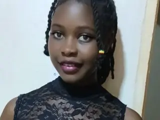 Smiling young Black woman with braided hair wearing a black lace top in a bright indoor setting.