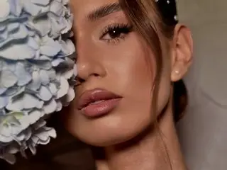 Sassy_starr poses close-up, showing her face, eyes, and lips with her long brown hair framing her face against a soft background.
