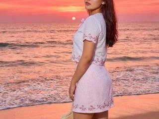Sassysoumya stands on a beach at sunset wearing a short white floral patterned dress.