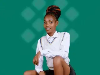 Smiling young African woman in a white school uniform sitting against a green patterned background.