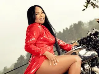 ScarletFerer poses outdoors in a red shiny latex dress, showing her long black hair and bare legs.