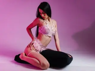 ScarletMore poses in white lace lingerie, showing her long black hair and bare skin against a purple background.