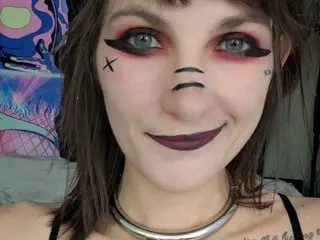 Scarlettshines smiles at the camera with dark eye makeup and black face paint markings on her nose and cheek.