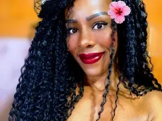 SelenaLove99 smiles with a pink flower in her long, curly black hair.