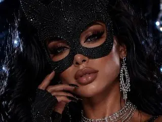 SerrenaOwner wears a black sequined mask and matching jewelry, posing with her hands near her face and long dark hair.