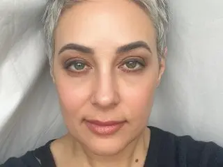Seska looks directly at the camera with a neutral expression, showing her short grey hair and light makeup against a plain white background.