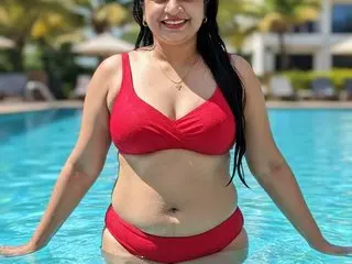 SexyRadha poses in a red bikini top, showing her cleavage and stomach, with her long black hair down in a bright outdoor setting.
