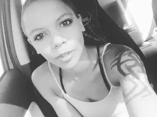 Smiling woman with tribal arm tattoo wearing a white tank top sitting in a car.