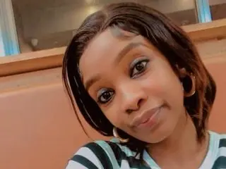 SexyYummyMia looks at the camera with a soft smile, showing her dark hair and hoop earrings while wearing a striped top.