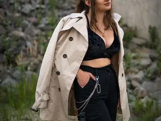 Sexyjiya77 poses in a tan trench coat over a black lace bra, showing her cleavage and dark hair against a soft, natural outdoor background.