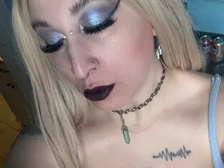 ShaeWednesday shows her face and shoulders with blonde hair, heavy blue eyeshadow, and a dark lip, wearing a black choker and a nose ring.