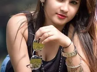 Shalini_Shalu poses with her long dark hair, wearing a black tank top and holding sunglasses near her chest.