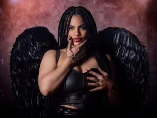 Glamorous woman in black corset and large black wings posing against a moody, dark red background.