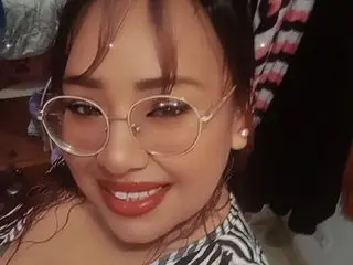 Sharaoz89 smiles with her long dark hair and red lipstick, wearing round glasses in a close-up headshot.