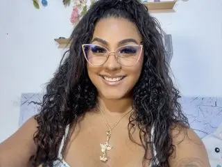 SharidCoronado smiles while wearing glasses and a white lace top, showing off her long, dark curly hair.