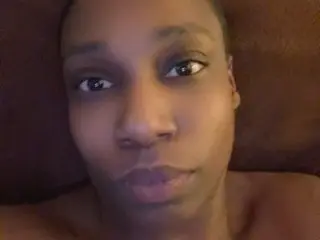 SheBooFreaky looks directly at the camera with a close-up headshot, showing her face and bare shoulders against a dark background.