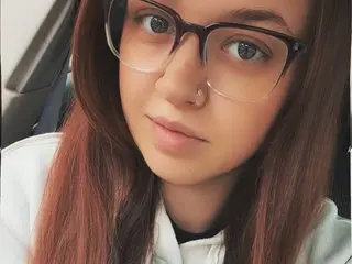SherriCola poses for a close-up selfie, showing her face, long brown hair, and clear glasses.