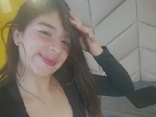 Smiling young woman with long brown hair and large hoop earrings wearing a black top in a bright room.