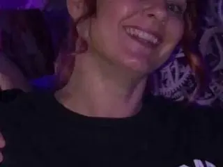 ShyMachXx smiles broadly, showing her teeth, with her hair pulled back and a dark shirt visible.