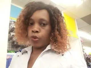 Smiling woman with curly brown hair wearing a white button-down shirt in a bright retail store setting.