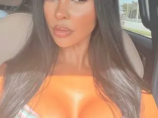 Shybuttcute poses close up, showing her long dark hair and cleavage in an orange top.