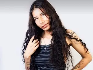 SienaBouer poses with long, wavy dark hair, wearing a black tank top against a plain white background.