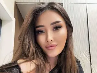 Silk_Siren poses with long brown hair and heavy eye makeup, looking directly at the camera in a close-up headshot.