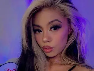 SilkyDanes poses with a direct gaze, showing her long blonde hair and facial features against a purple background.