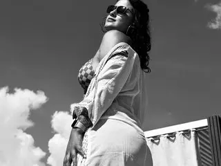 Stylish woman in sunglasses and white summer outfit posing under a bright sky in a dreamy black and white mood.
