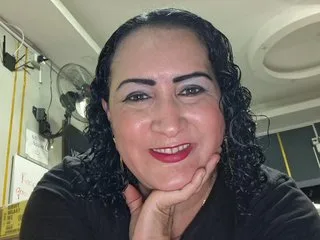 SilverCougarr smiles at the camera with her dark curly hair and red lipstick, resting her chin on her hand.