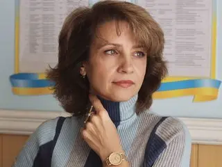 SimplyEnchanting poses with a direct gaze, wearing a light blue turtleneck, her brown hair styled in a soft bob.