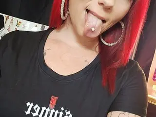 SindraSinner poses in a black t-shirt, showing her red hair and a close-up of her mouth with her tongue out.