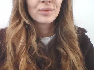 SinnerBunny shows her long brown hair and smiling face while wearing a dark brown zip-up jacket against a plain white background.