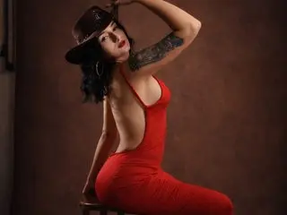 SisiRojass poses in a red backless dress, showing her bare back and side, with her dark hair styled in a bob and a large tattoo on her upper arm.