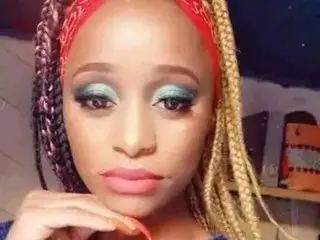 Woman with colorful braids and glamorous teal eyeshadow posing with a serene expression indoors.
