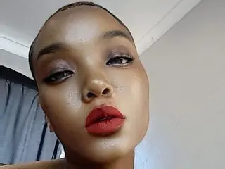 Close-up portrait of a woman with glowing skin and bold red lipstick posing in a bright indoor setting.