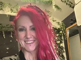 SkySparks smiles at the camera, showing her long red hair and face in a close-up shot.