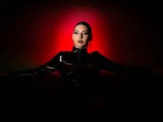 Elegant woman in a black latex outfit posing against a dramatic red glowing background with a moody atmosphere.