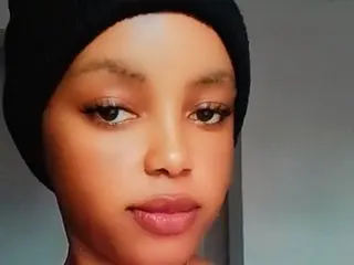 Smalldoll looks directly at the camera with a neutral expression, showing her face and dark hair tucked under a black beanie.