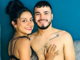 SoffiaKonig smiles while posing shirtless, showing her bare chest and black bra strap against a blue background.