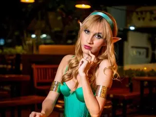 SofiLopezzz20 poses in a teal bra and matching headpiece, looking at the camera with her hand near her chin in a dimly lit room.