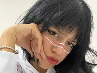 Sofi_shadow poses with her hand against her cheek, showing her dark hair and red lipstick in a close-up shot.