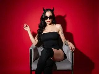 SofiaGale wears black sunglasses and devil horns while posing in a black bodysuit against a red background.