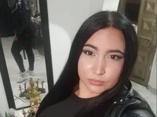 Sofia_SyS has long black hair and wears a black leather jacket, posing close-up against a white wall.
