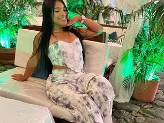 Sofiawelss poses with her hand near her face, wearing a white patterned bra and matching bottoms while sitting on a white lounge chair.