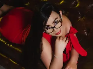 Elegant woman in a red dress and glasses relaxing on a dark leather sofa with a moody, sophisticated vibe.
